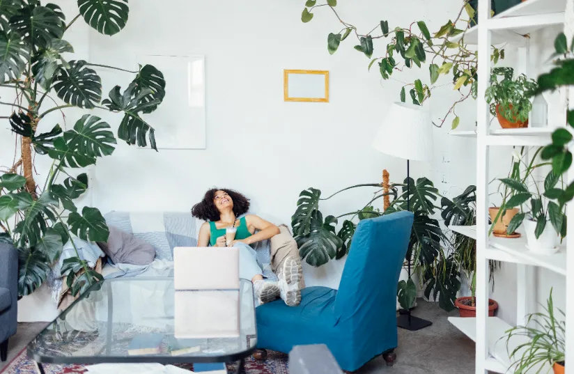 A woman sitting in the sofa while smiling on the plants in the house.