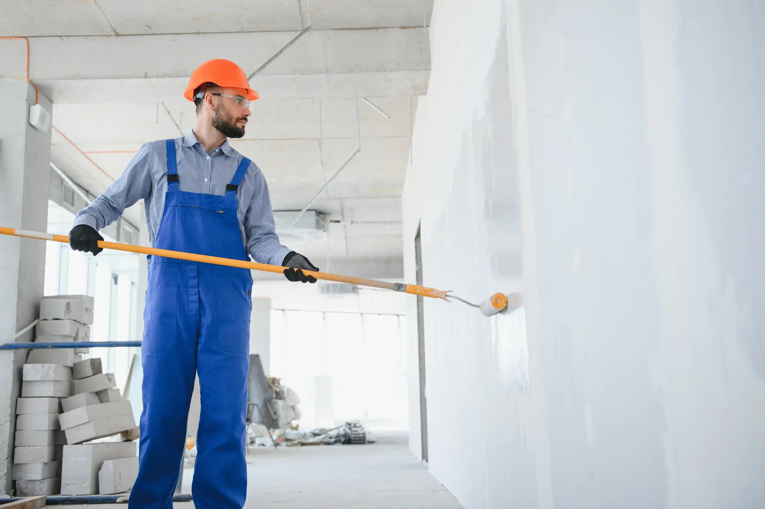 A worker in an overall painting the wall.